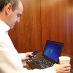 Man logging in on a laptop while holding a smartphone
